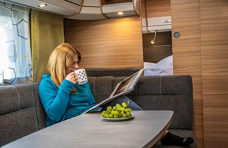 A guest sits in the caravan, drinking coffee and reading